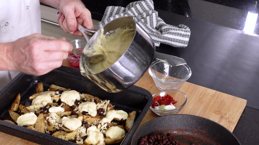 Cheese sauce being poured over oven-baked potato wedges