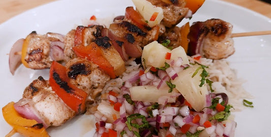 Jerk chicken skewers resting on a bed of rice and peas, topped with fresh pineapple salsa