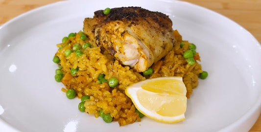 Finished chicken paella in the pan with a chicken thigh sitting on top of the rice