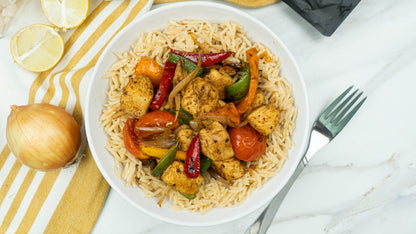 Bowl of moroccon tagine chicken with vegetables on a bed of rice, garnished with lemon wedges and an onion.